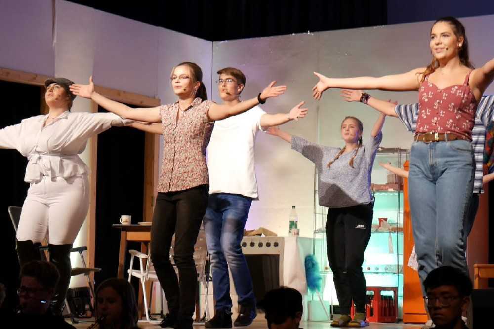 None - Fünf Darsteller die versetzt zueinander stehen und ihre Arme nach außen strecken auf der Bühne